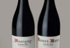 Two wine bottles side by side with red capsule tops and white Grand Cru labels showing vintages 2014 and 2018 (Musigny and Bonnes-Mares).