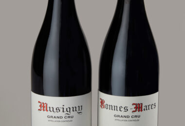 Two wine bottles side by side with red capsule tops and white Grand Cru labels showing vintages 2014 and 2018 (Musigny and Bonnes-Mares).